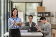 © ArLawKa - A female Asian accountant stands in front of a desk and two businessmen meet to discuss brainstorming, calculations, and joint analysis of the company's growth goals.