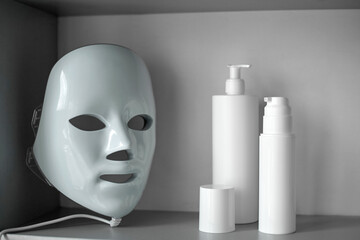 Light therapy LED mask on a shelf next to facial skin care products.