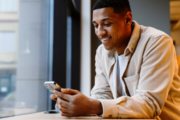 Wall Mural - Cheerful guy using smartphone online mobile app while sitting in office