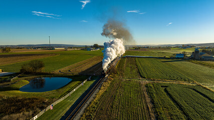 Canvas Print - An Aerial View at Sunrise of a Steam Passenger Train Approaching Blowing A Lot of Smoke on a Autumn Day