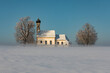 Bavarian church of Raisting with trees and snow and mist during winter, snow field in the foreground, blue sky day, Bavaria Germany.