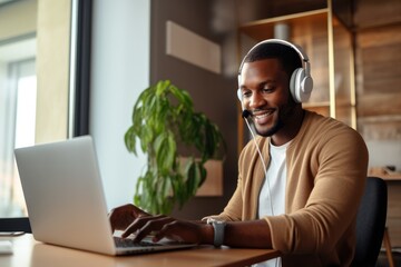 Aufkleber - A focused man sits at his desk in an office building, surrounded by furniture and a houseplant, wearing headphones and a smile while working on his laptop