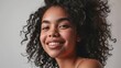 © BackgroundHolic - Close up studio shot of beautiful young mixed race woman model with curly dark hair looking at camera with charming cute smile while posing against white blank copy space wall for your content