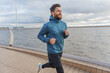 © muse studio - Focused man in sportswear running along the waterfront, with urban skyline in the background