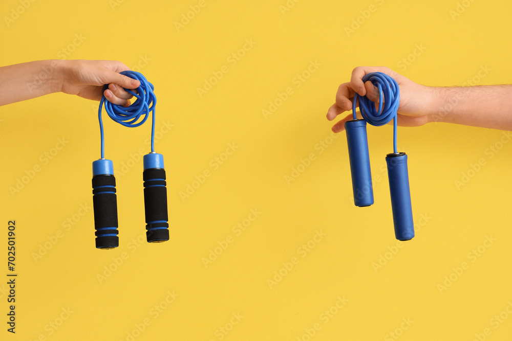 Female hands with skipping ropes on yellow background