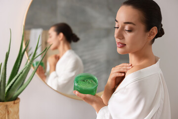 Wall Mural - Young woman applying aloe gel onto her shoulder near mirror in bathroom