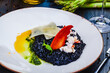 Black squid ink risotto with lobster and parmesan cheese on white plate.
