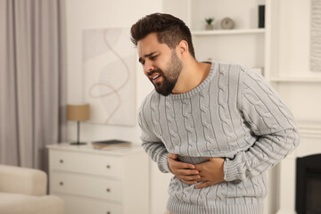 Wall Mural - Young man suffering from stomach pain indoors. Space for text