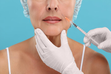 Wall Mural - Doctor giving facial injection to senior woman on light blue background, closeup. Cosmetic surgery