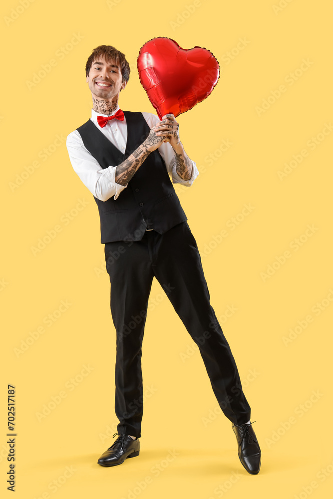 Handsome young man with heart-shaped air balloon on yellow background. Valentine's day celebration