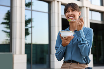 Wall Mural - Happy businesswoman with plastic bowl of salad having lunch outdoors