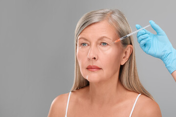 Wall Mural - Doctor giving facial injection to senior woman on light grey background, closeup and space for text. Cosmetic surgery