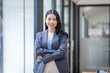 © David - Young happy business asian woman with arms crossed standing int her office and looking at camera.