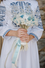 Wall Mural - Wedding bouquet flowers on background stylish bride. A woman wearing an embroidered dress holds a bouquet. Wedding ceremony outdoors. Closeup.