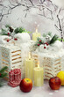 New Year's decoration in the form of white wooden boxes with bows and fir branches. Candles and fruits for the holiday.