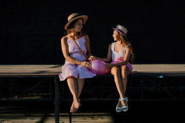 Wall Mural - mother and daughter are sitting in pink dresses with flowing long hair on a black background. Enjoy communicating with each other