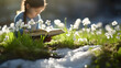 Child reading a book on a meadow with flowers and grass growing through the melting snow. Concept of leisure activity, spring coming and winter leaving.