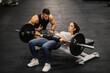 A fit sportswoman is doing workouts for core and abs with barbell in a gym with her trainer.