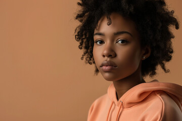 Wall Mural - African American serious teenage girl wearing hoodie on peach background