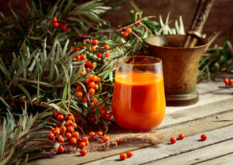 Wall Mural - Glass of sea buckthorn juice with fresh berries on an old wooden table.