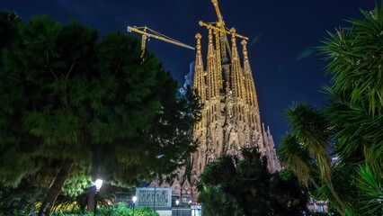 Wall Mural - Timelapse Hyperlapse of the Illuminated Top of Sagrada Familia in Barcelona, Spain. Spires and Cranes Grace the Skyline, Offering a Majestic View from the Tranquil Park