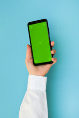 Wall Mural - Hand in a white shirt holding a phone with a green screen on a blue background