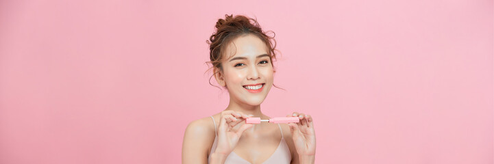 Wall Mural - Young woman using lip gloss looking at camera on pink studio background