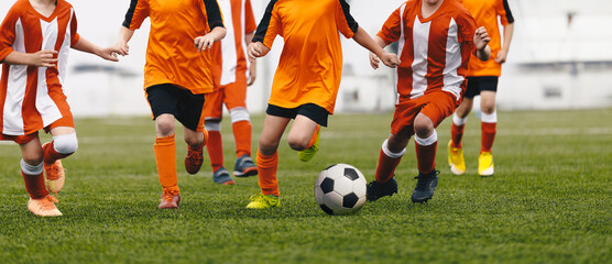 Wall Mural - Cchildren having fun in soccer football game. Group of school kids running ball in football duel. School boys in sports outdoor competition. Children in red and orange soccer uniforms