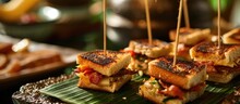 Restaurant service featuring bite-sized grilled cheese and bacon sandwiches on bamboo toothpicks and banana leaf garnish.