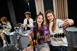 © LIGHTFIELD STUDIOS - focus on jolly teenage girls taking selfie and singing with blurred friends playing instruments