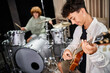 © LIGHTFIELD STUDIOS - focus on talented adorable teenage boy playing guitar actively next to his blurred drummer in studio