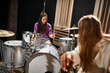 jolly adorable teenage girl playing drums while her blonde friend looking at her, musical group