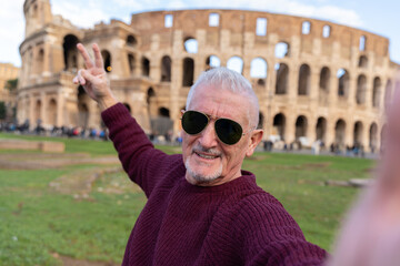 happy middle aged man on vacation taking a selfie in front of coliseum amphitheatre in rome