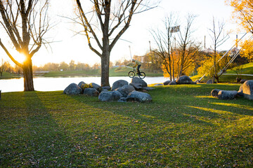 Parklandschaft im Herbst in München. Wiese, bunte Bäume und große Steine, auf denen ein Mountainbiker übt. Ein See im Hintergrund