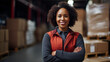 Black woman Logistic worker with no hat standing and a red uniform smiling at the camera on a warehouse background