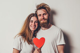 Fototapeta Panele - Portrait of beautiful cheerful couple holding two red paper hearts on solid background. Celebrating Valentine's day.