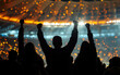 Silhouettes of cheering crowd in front of a large football stadium