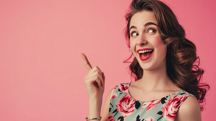 Attractive young woman with dark hair smiles tootiy points away on blank space gives suggestion or recommendation wears rose print shirt advertises product isolated over coral pink background