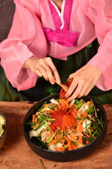 Kimchi preparation. A young Korean woman wearing a pink hanbok is pouring Korean chili powder into a bowl of vegetables for making kimchi. which is a national food preservation