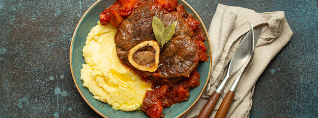 Wall Mural - Traditional Italian dish Ossobuco all Milanese made with cut veal shank meat with vegetable tomato sauce served with corn polenta on ceramic plate top view on rustic stone background.