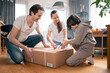Son, dad and mom, together eagerly unpack a large cardboard box from a parcel with goods that were delivered to their home. Shopping online with home delivery of orders.