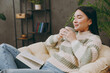 Side view young calm smart fun woman wear casual clothes sits on armchair read book novel drink tea stay at home hotel flat rest relax spend free spare time in grey living room indoor. Lounge concept.