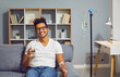 © Studio Romantic - Young happy african american man sitting on the couch in the clinic holding a glass of water while receiving IV drip infusion and vitamin therapy in his blood. Person receiving injection therapy.