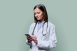 © Valerii Honcharuk - Young female doctor using smartphone, on green studio background