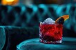 Indulge in the refreshing taste of a vibrant red cocktail, garnished with a juicy slice of orange and a single ice cube, perfect for a cozy indoor gathering