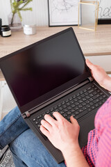 Man typing on laptop and surfing web from home. Side view of man using his laptop screen blank, mockup screen. Freelancer working on laptop at home. 