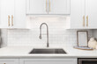 A kitchen faucet detail with white cabinets, gold hardware, and a subway tile backsplash.