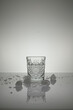 Vertical shot of crystal water glass, ice cubes and waterdrops around, on a white shiny surface