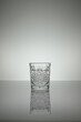 Crystal water glass reflecting on a gray surface with white background