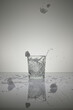 Vertical shot of ice cubes falling into a crystal water glass,isolated on a wet shiny white surface